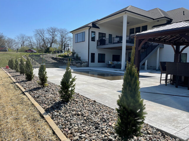 large boulder retaining wall with garden border with rocks and small evergreen trees